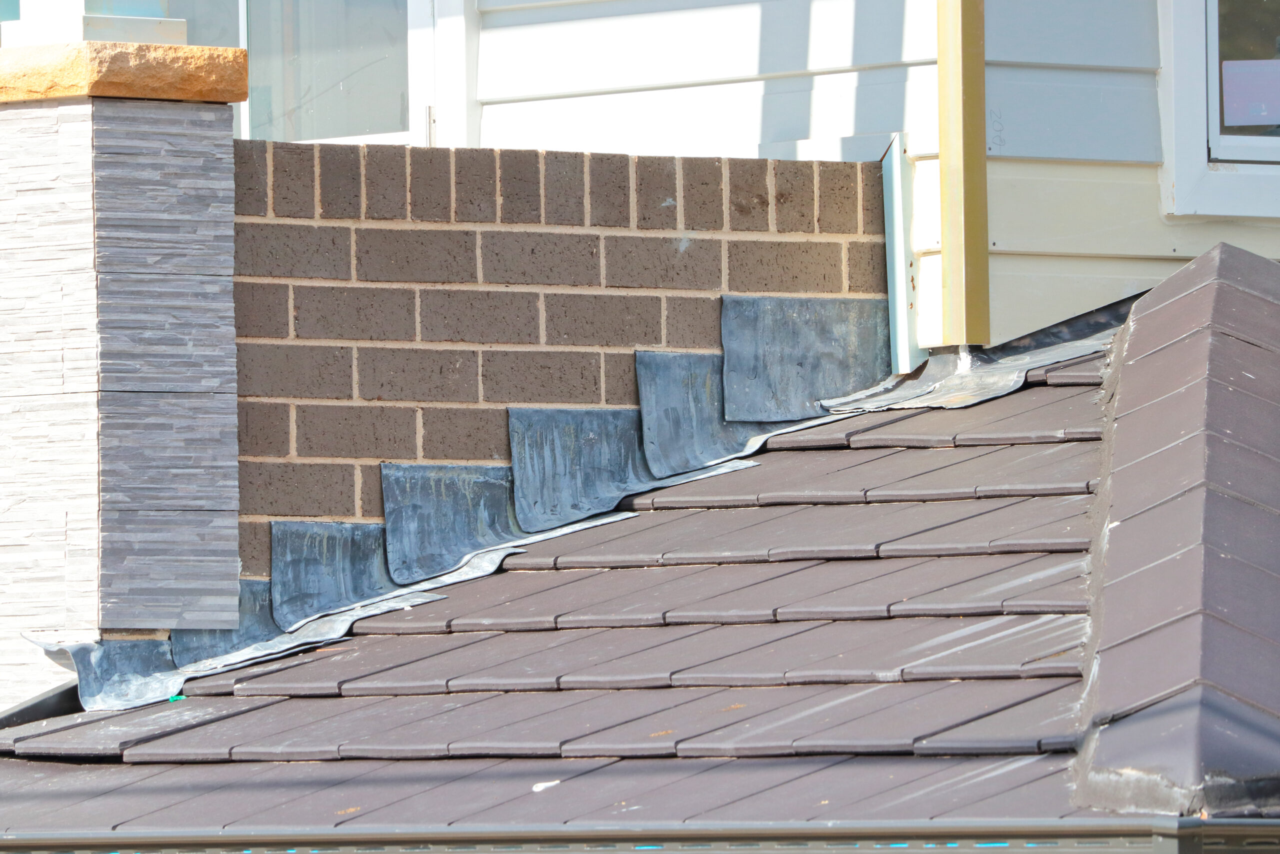 Roof flashing installed along the intersection of a brick wall and shingled roof to prevent water leakage.
